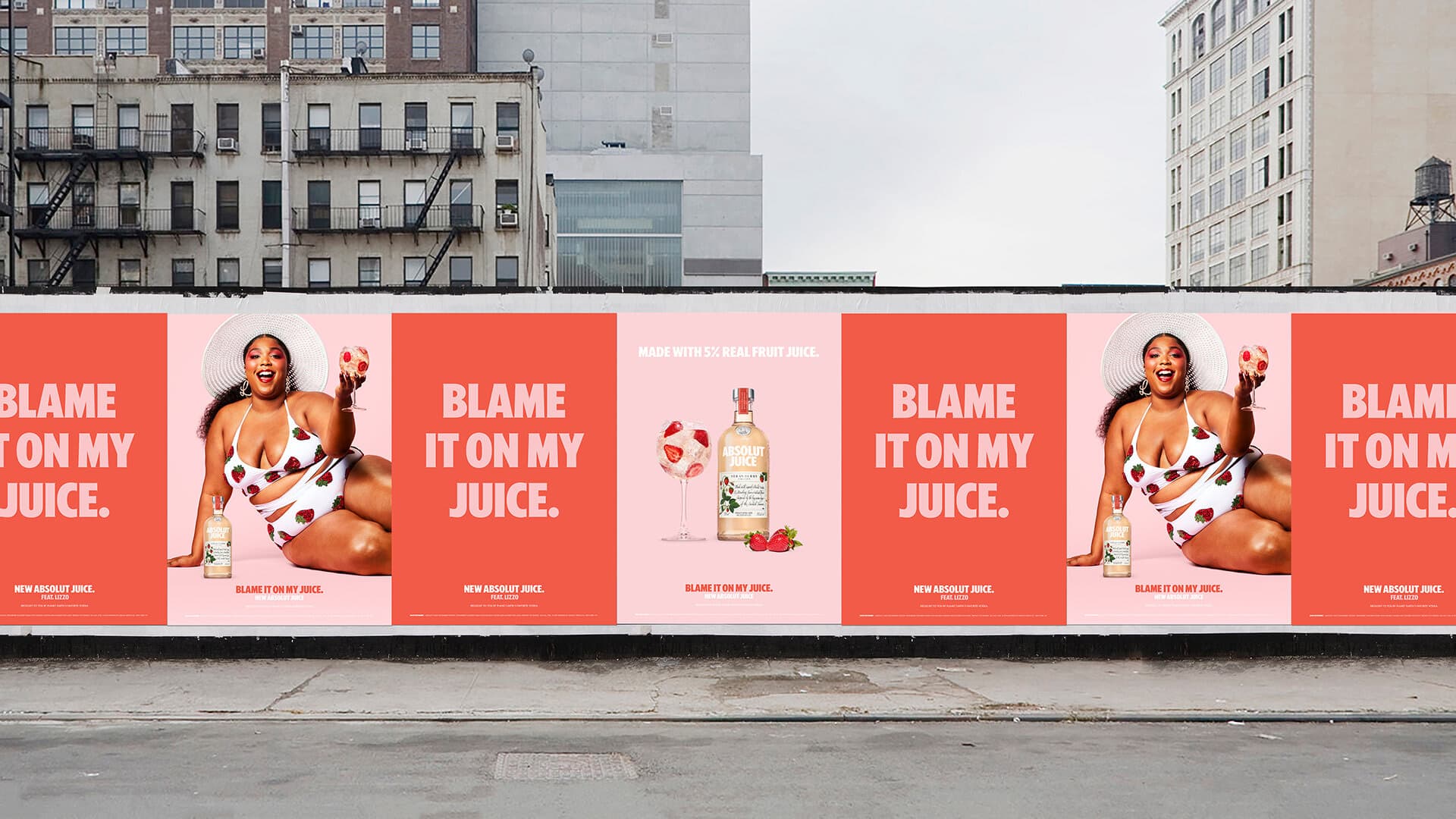 Wide street-level photo of a city wall lined with a run of red and pink OOH posters: alternating 'BLAME IT ON MY JUICE.' type posters, Li…