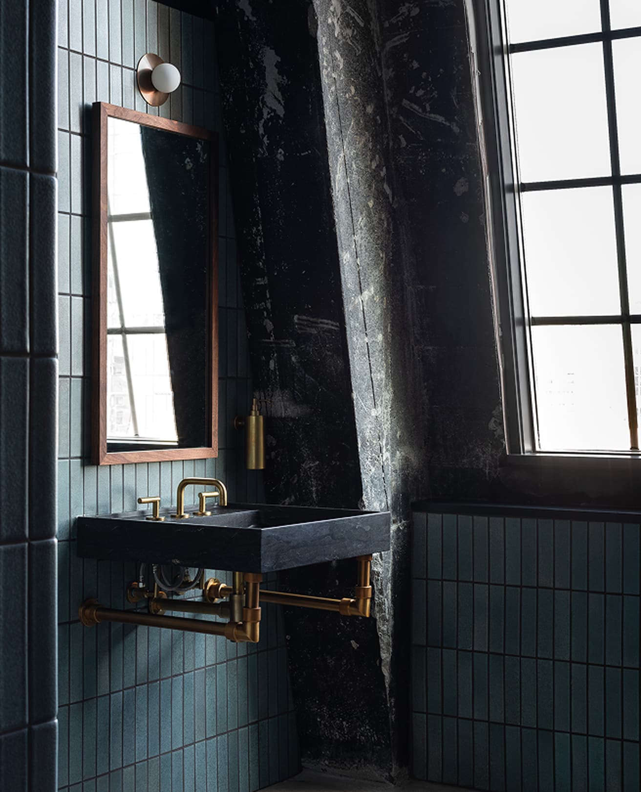 Blue-tiled bath corner with a black stone sink on exposed brass plumbing