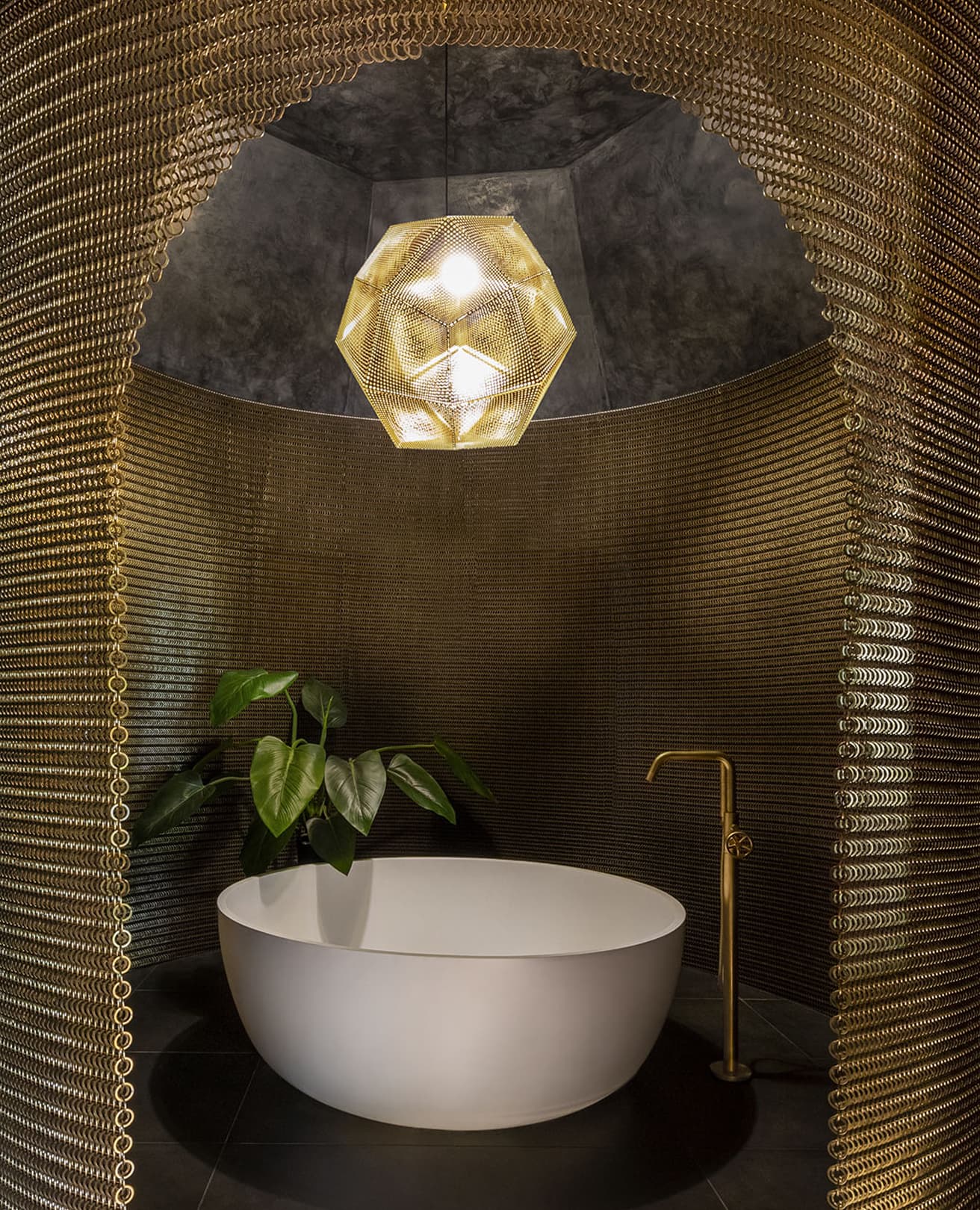 Round white tub beneath a brass chainmail arch and geodesic pendant