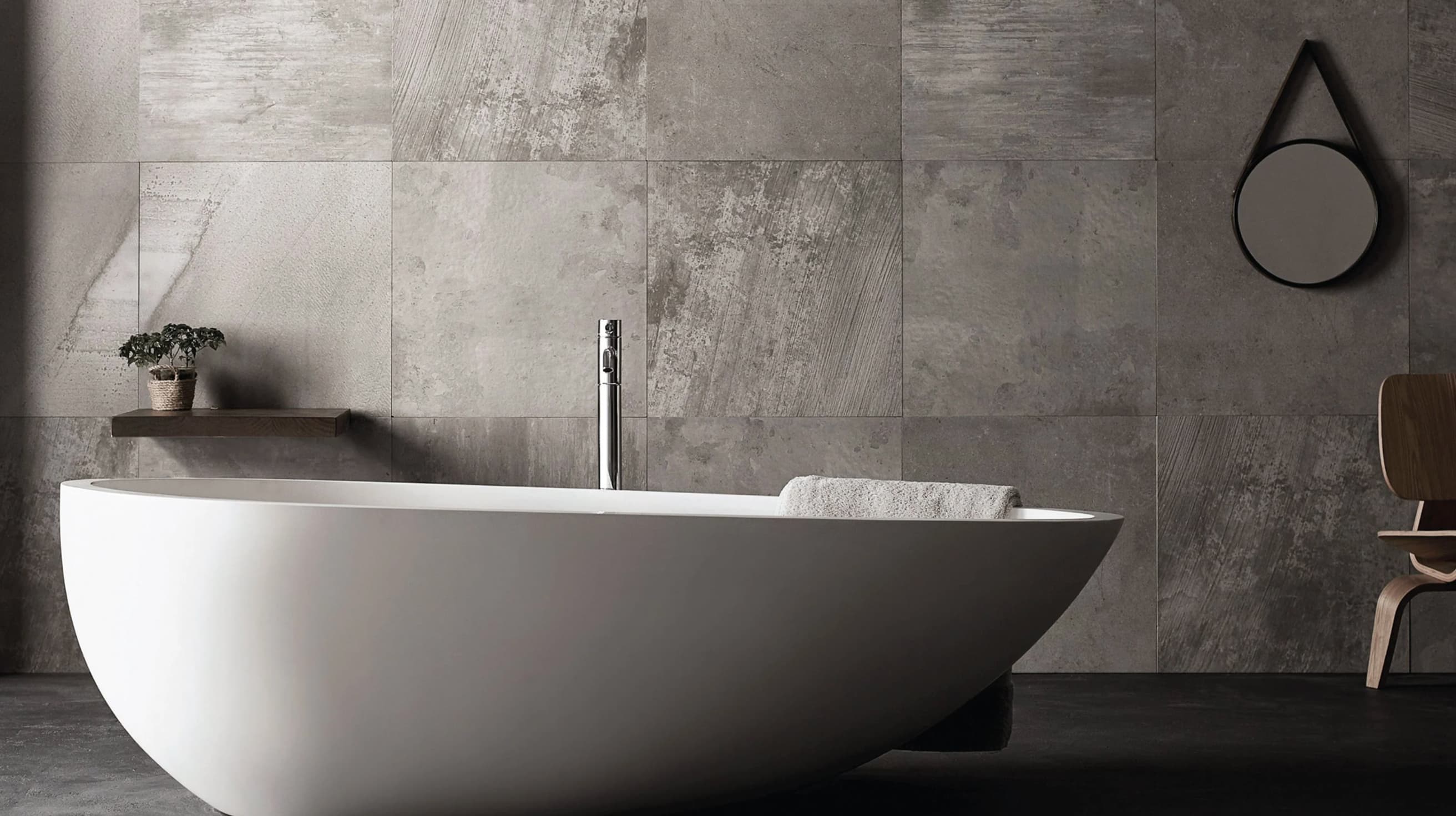 Wide grey stone bathroom with a white egg-shaped freestanding tub, chrome floor-mounted filler and a round hanging mirror