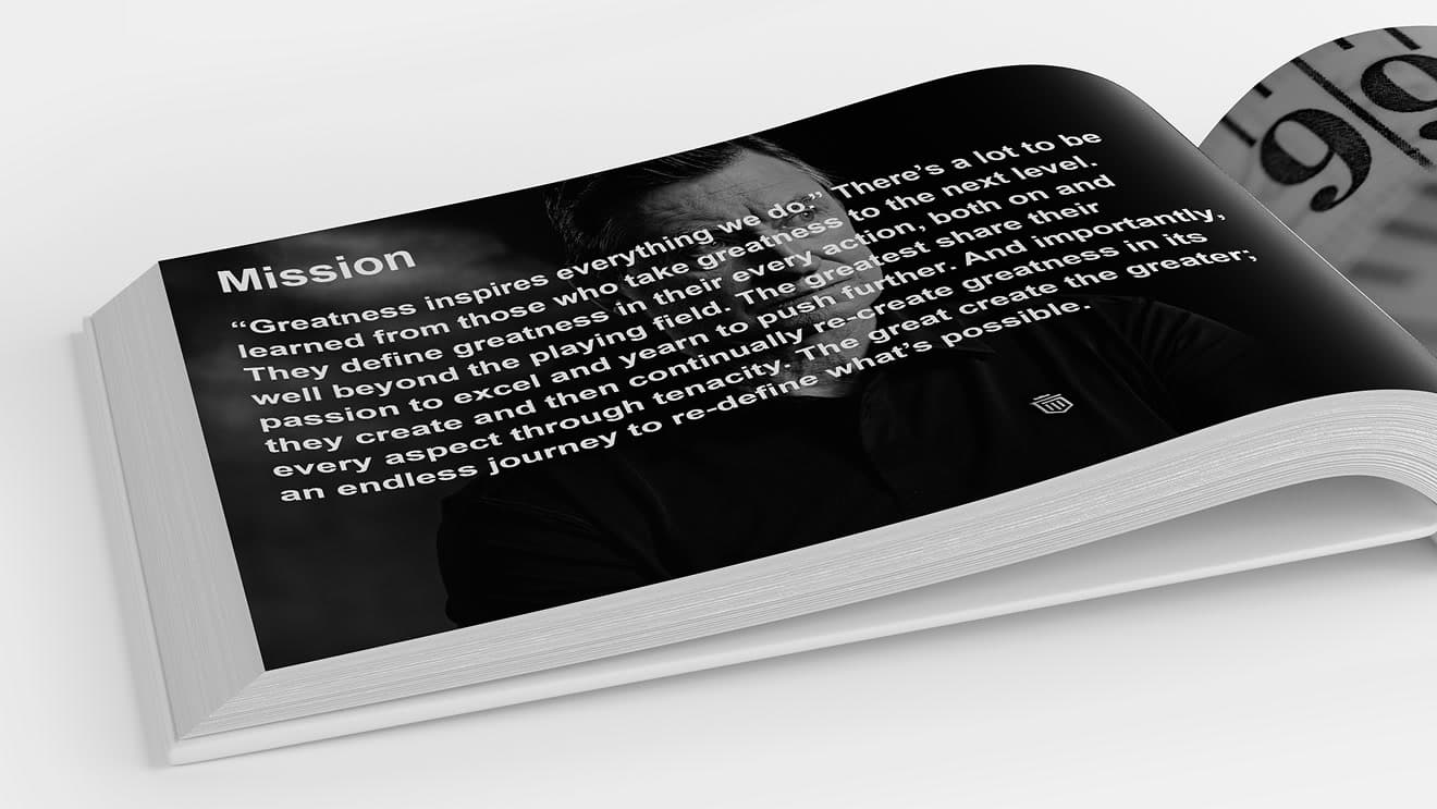 Photographed mockup of a printed brand book open on a white surface, spread showing a black page headed 'Mission’ with the manifesto copy…