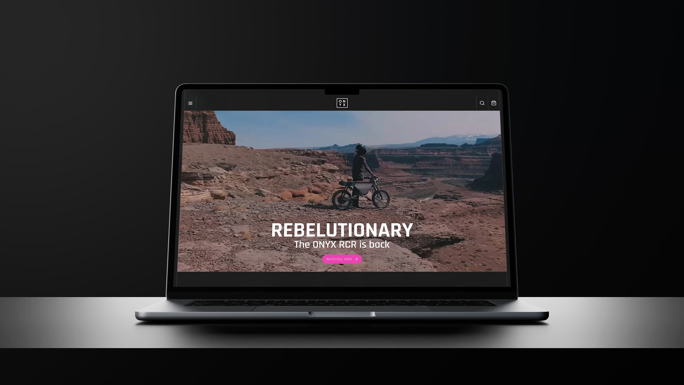 Laptop mockup on a dark reflective surface showing the Onyx homepage hero: a rider on rocky desert terrain with the overlay 'REBELUTIONAR…