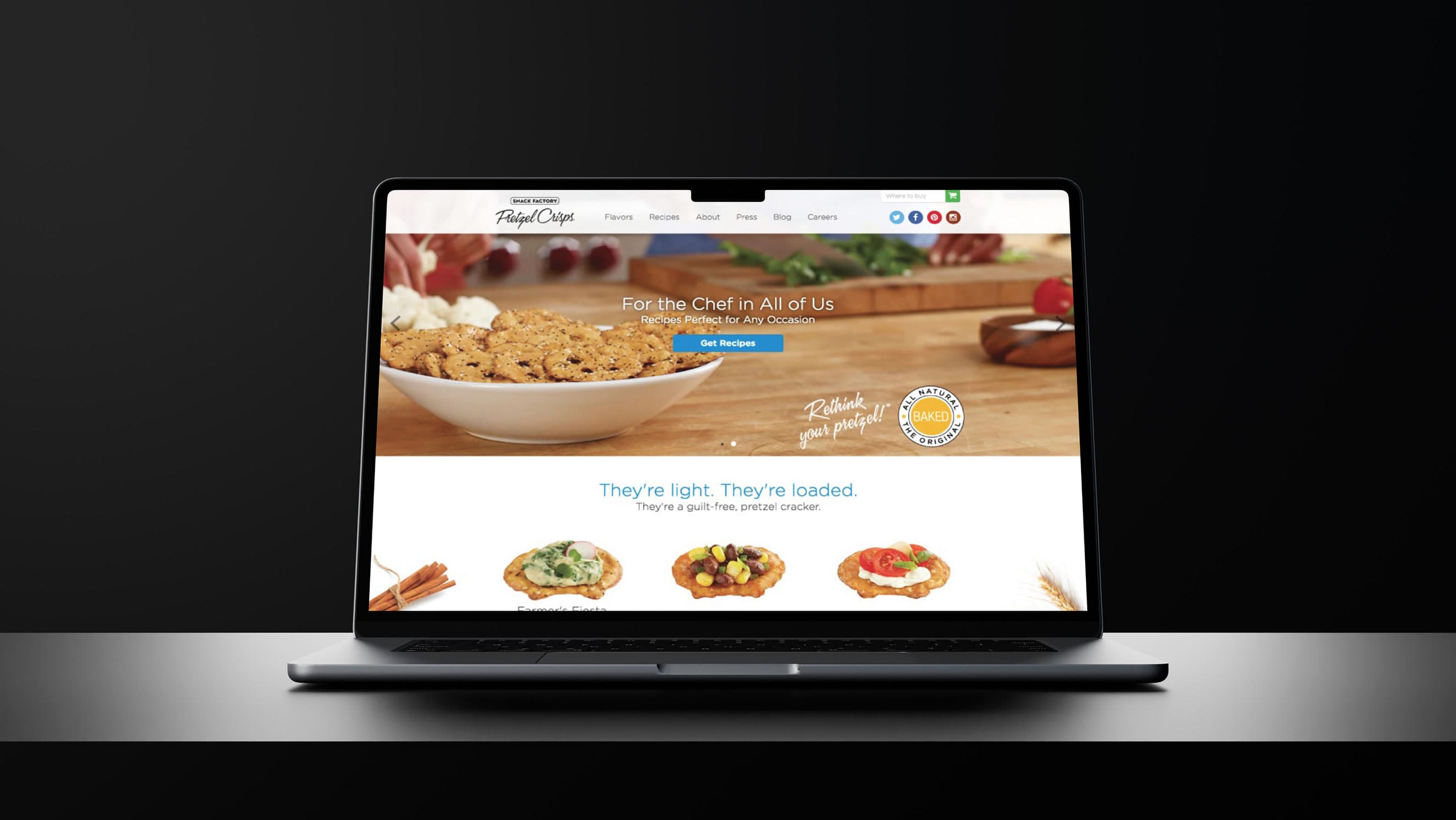 Laptop mockup on a dark reflective surface showing the Pretzel Crisps homepage — hero band reading 'For the Chef in All of Us / Recipes P…