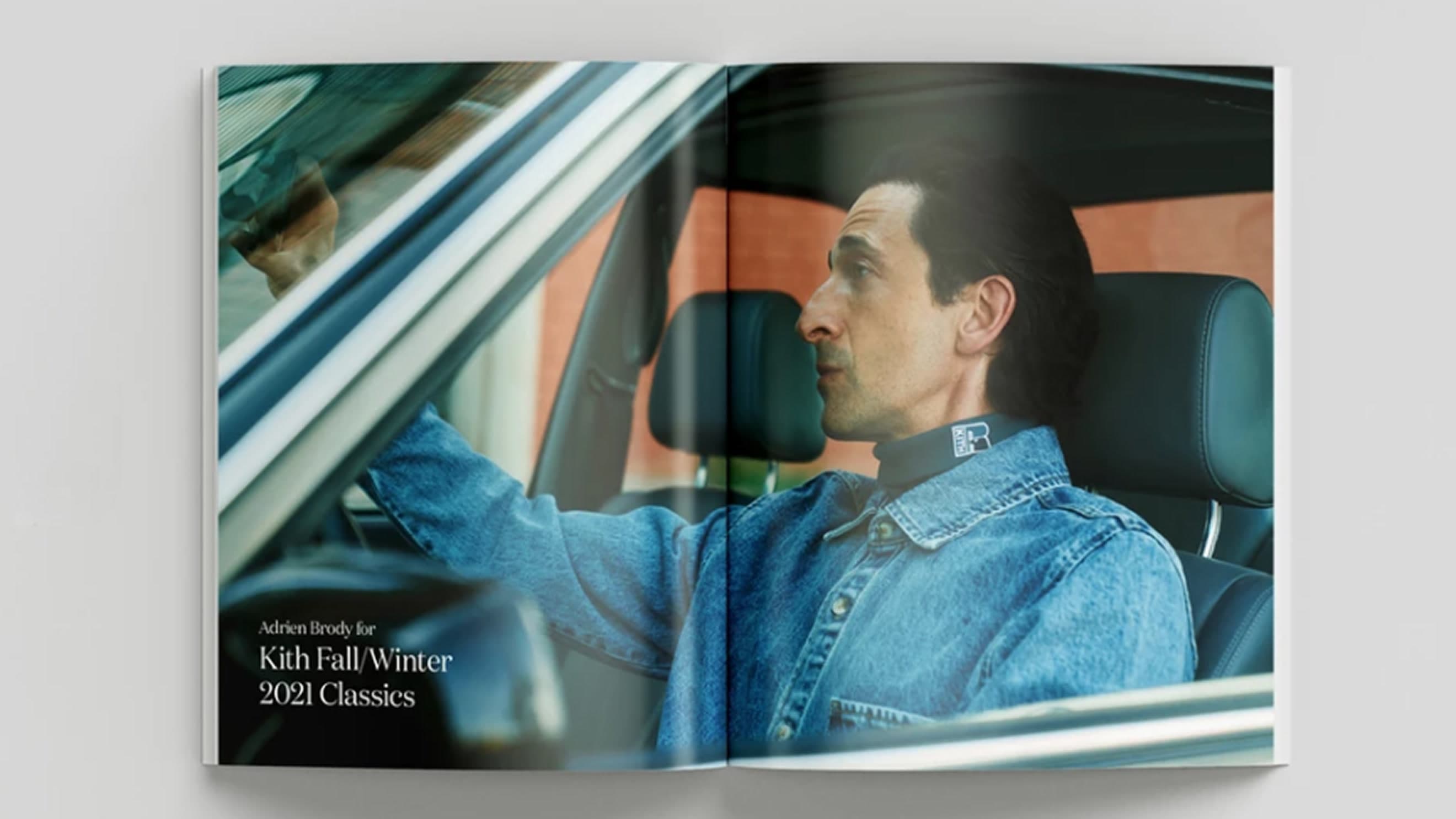 Full-width photo of an open magazine/lookbook spread laid on a light grey surface — Adrien Brody in denim seated in a car, wearing a Kith…