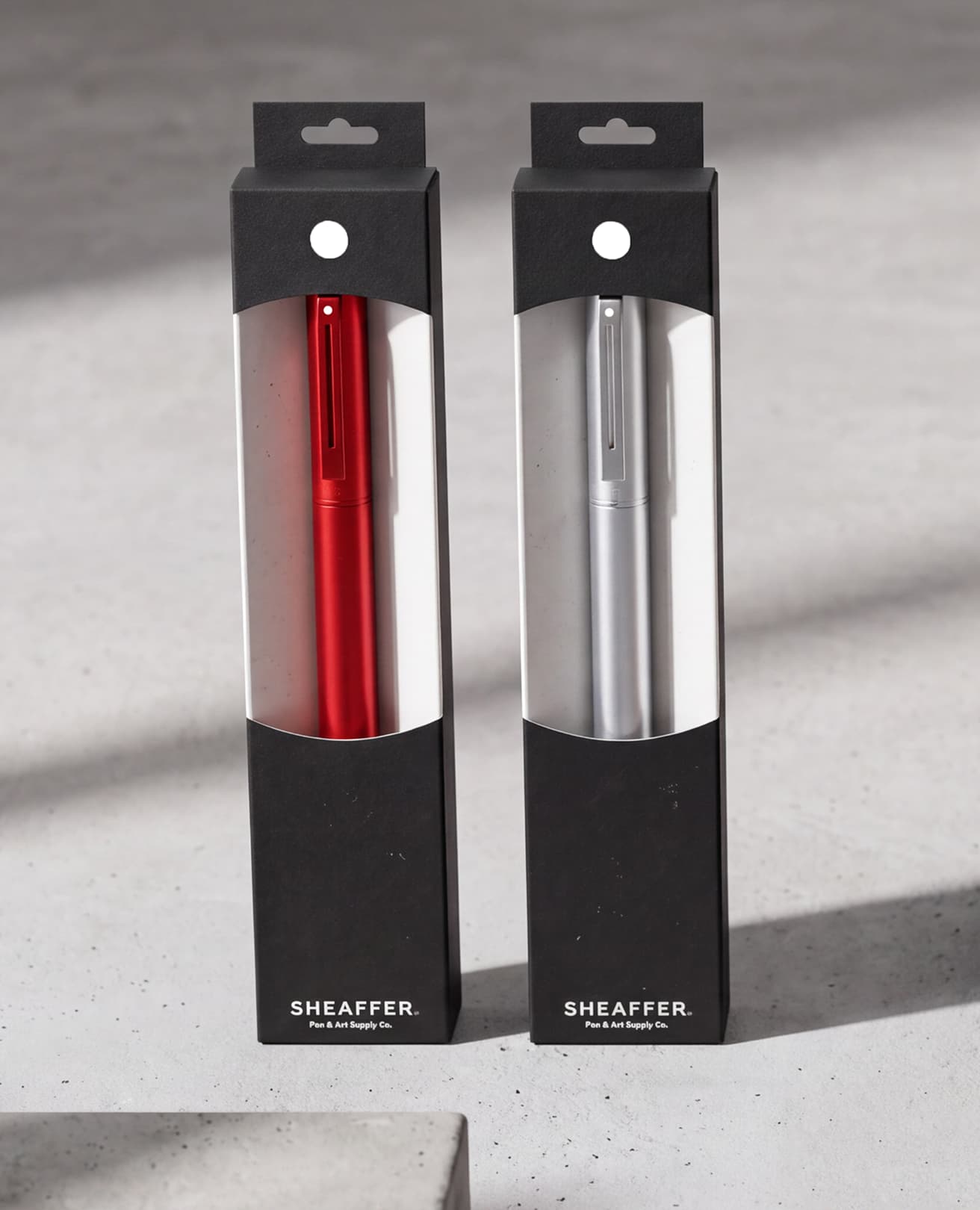 Red and silver Sheaffer pens in windowed black boxes on concrete