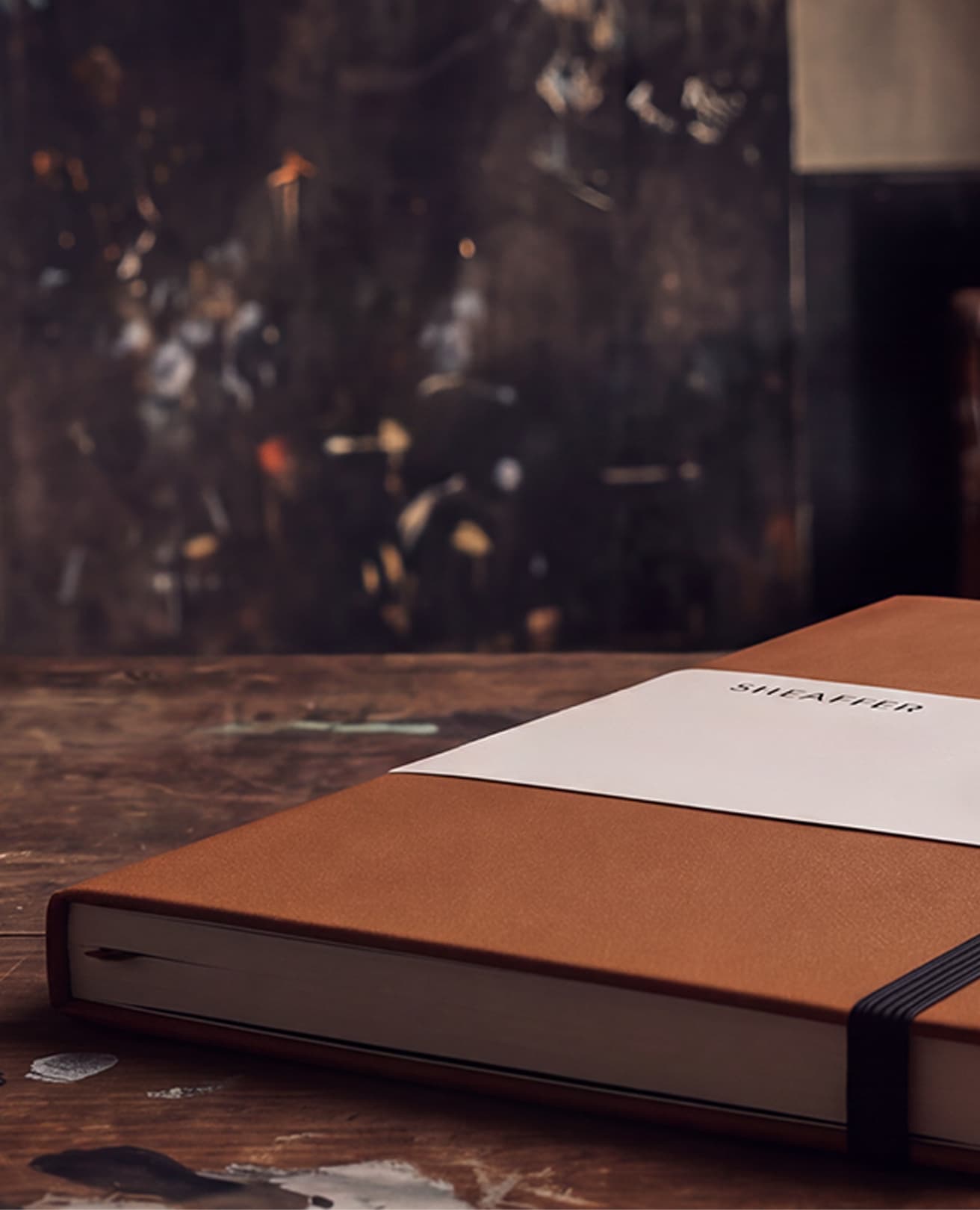 Tan Sheaffer notebook with a white belly band on a worn wooden desk