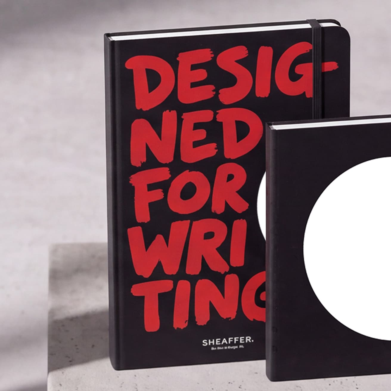 Two black Sheaffer notebooks, one covered in red brush lettering reading 'Designed for Writing', one with a large white dot (2 of 2)