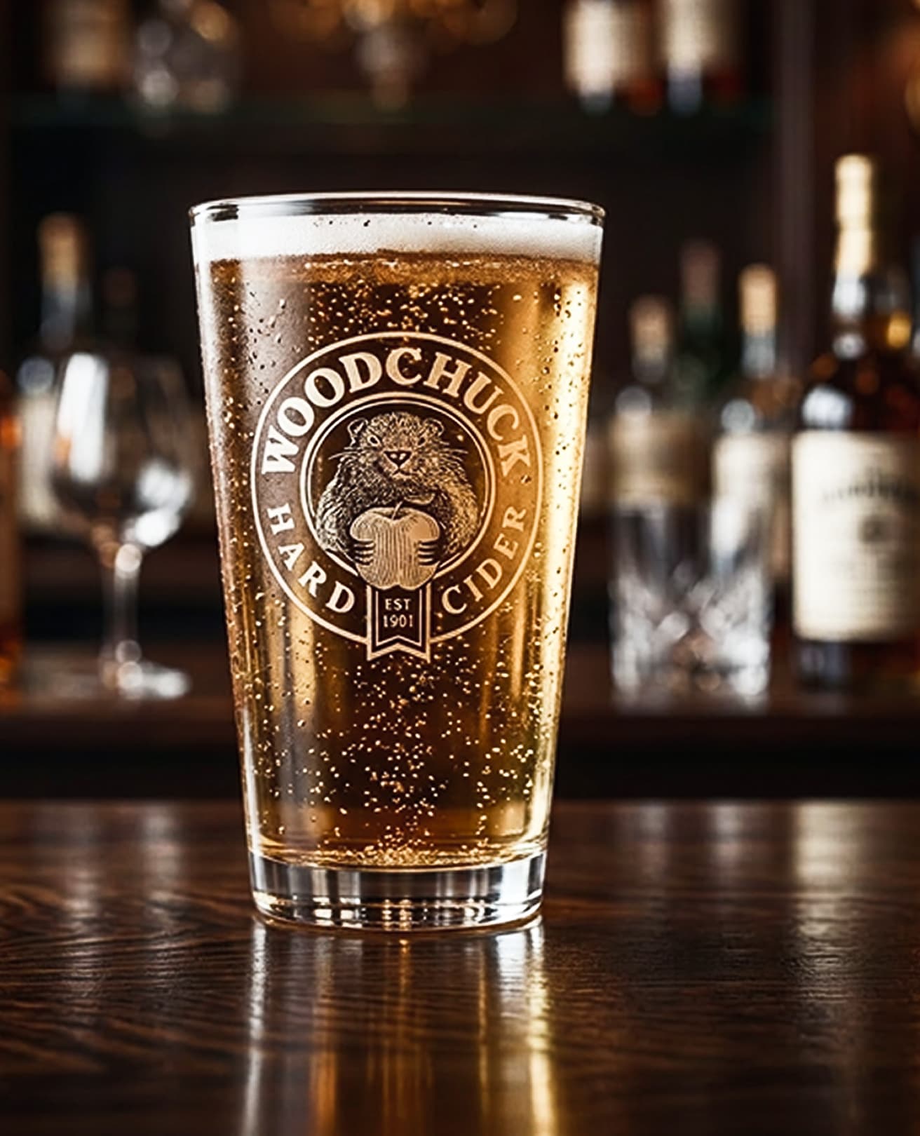 Pint glass of cider etched with the Woodchuck roundel on a bar top
